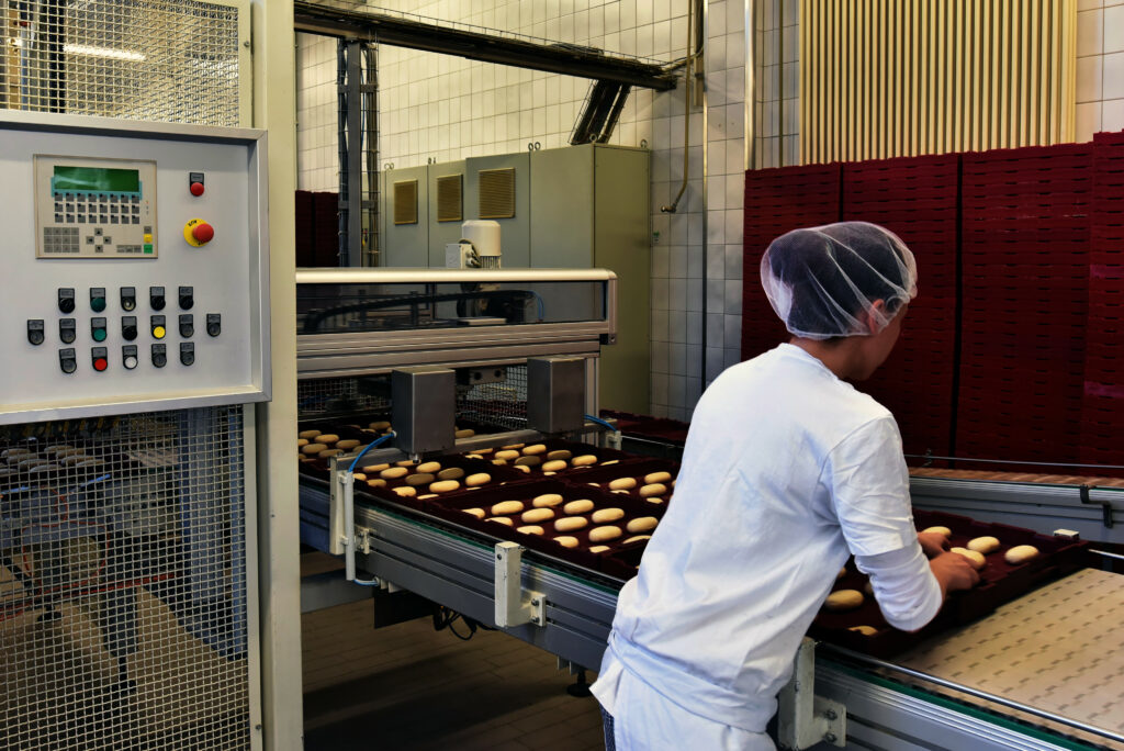 Frau arbeitet am Fliessband einer Großbäckerei // Woman is working on the conveyor belt of a bakery
