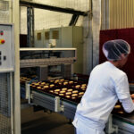 Frau arbeitet am Fliessband einer Großbäckerei // Woman is working on the conveyor belt of a bakery
